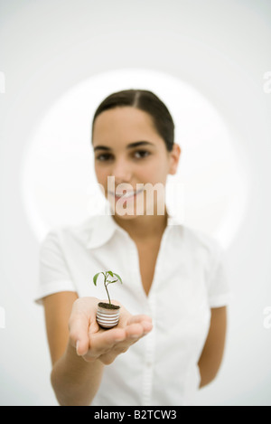 Teengirl halten Setzling gepflanzt in Glühbirne Basis, lächelnd in die Kamera Stockfoto