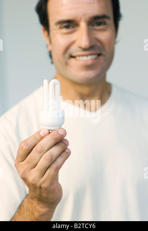 Mann hält Energie effiziente Glühbirne, lächelnd in die Kamera Stockfoto