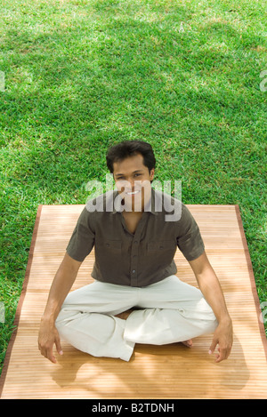 Mann sitzt mit gekreuzten Beinen im Freien, lächelnd in die Kamera, erhöhte Ansicht Stockfoto
