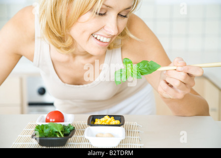 Lächelnde Frau beugte sich über, mit frischem Basilikum mit Stäbchen, Stockfoto