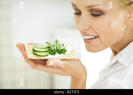 Lächelnde Frau hält Cracker mit Gurkenscheiben, Stockfoto