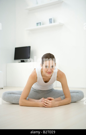 Dehnung auf dem Boden, in die Kamera lächelnde Frau Stockfoto