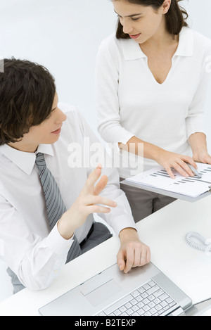 Fachleute diskutieren, Graph, weibliche stehen und halten Zwischenablage, männliche sitzen und Geste Stockfoto