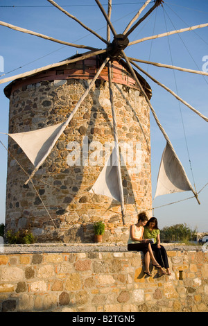 Zwei Frauen vor einer Windmühle sitzen und lesen ein Buch, Antimachia, Kos, Griechenland Stockfoto