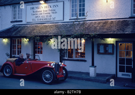 Zwei Mann fahren eines Oldtimers vor dem Drunken Duck Inn, Lake District, Cumbria, England Stockfoto