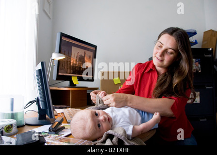 Multitasking-Frau, die Mutter arbeitet jongliert Arbeit im Home Office und wechselnden Baby auf ihrem Schreibtisch Stockfoto