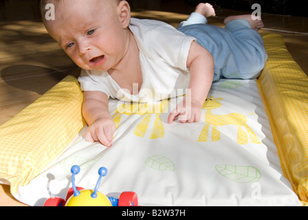 Baby Boy auf Änderung in Frustration für Toy Spider Matte Weinen auf Bauch liegend Stockfoto
