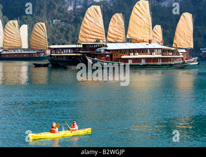 Kanuten paddeln vorbei an touristischen Kreuzfahrt Dschunken Halong Bucht Vietnam Stockfoto