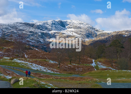 Wanderer auf Pfad um Tarn Hows mit Schnee bedeckt Wetherlam im Hintergrund Stockfoto