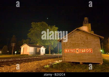 Ein Zug nähert sich das kleine Depot und Getreidesilo in der Innenstadt von Danforth, IL, erhellen die Nacht. Stockfoto