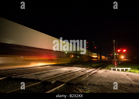 Eine intermodale Zug voller Container und Trailer Geschwindigkeiten an einer Kreuzung mit wartenden Autos vorbei. Stockfoto