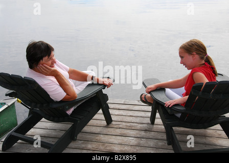 Großmutter und Enkelin sitzen in Adirondack Stühle auf einem Dock ein Gespräch Stockfoto
