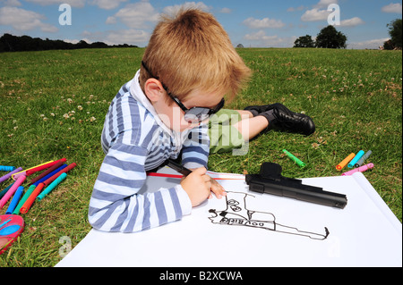 Horizontales Bild eines kleinen Jungen zeichnen ein Bild von seiner Spielzeugpistole im Park an einem Sommertag in Kent England Stockfoto