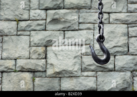 Ein großer Haken aus Metall an einer dicken Kette hängend vor einer Wand Schiefer Stockfoto