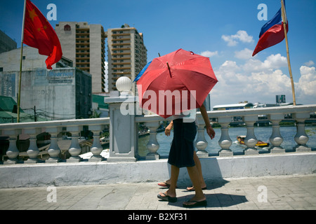 Ein paar schützen sich vor der Mittagssonne mit Sonnenschirmen und Überquerung des Pasig Flusses auf einer Brücke in Manila, Philippinen. Stockfoto