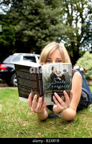 Junge Frau draußen im Park oder im Garten liegen auf ihrem Bauch auf dem Rasen, lesen ein Buch Modell veröffentlicht Stockfoto