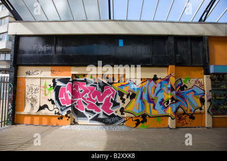 Graffiti auf Arcade von Geschäften unter einem Turm Wohnblock in Margate Kent Stockfoto