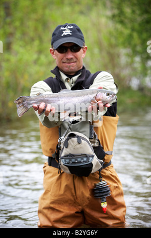 Ein Fischer steht in einem Fluss hält eine Forelle auf dem Display. Stockfoto