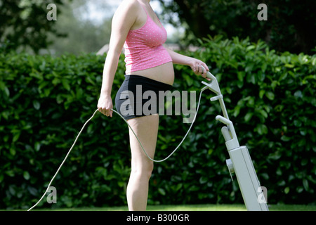 Schwangere Frau Rasenmähen mit Vakuum-Reiniger Stockfoto