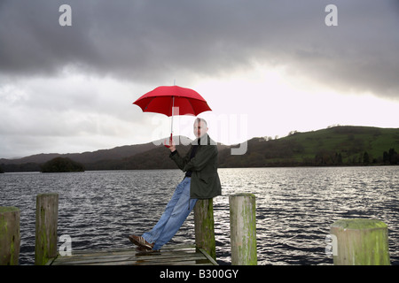 Mann am Dock in Regen, Windermere, Cumbria, England Stockfoto