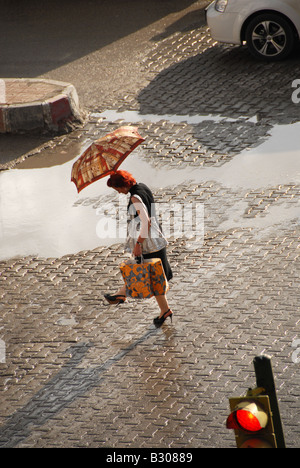 Frau, überqueren eine Kreuzung mit einem Regenschirm nach einer Dusche Stockfoto