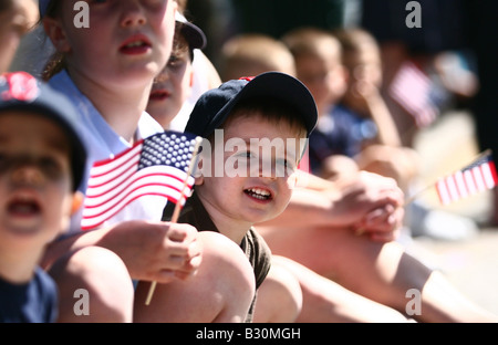 Ein All-American Boy lächelt, als er eine Memorial Day Parade in eine Heimatstadt Uhren mit amerikanischen Flaggen wehten.  Andere Kinder beobachten. Stockfoto