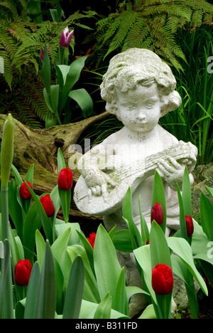 Statue eines Kindes spielt eine Gitarre unter roten Tulpen Stockfoto