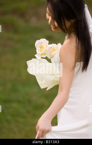 Eine schöne asiatische Braut hält ein Bouquet von zwei gelben Rosen, wie sie posiert im freien Stockfoto