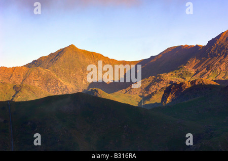 Der Gipfel des Mount Snowdon, beleuchtet von der aufgehenden Sonne, mit der Piste senkt Silhouette im Vordergrund Stockfoto