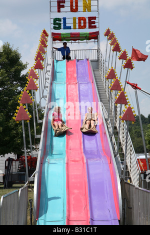 Zwei junge Mädchen rutschen ein hügelig geschwungenen Folie auf Entlassung auf Kirmes Jahrmarkt. Stockfoto