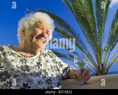 Unabhängige ältere Dame entspannt zufrieden in der Sonne mit einem Glas Weißwein in ihrer Ferienvilla nach Hause Stockfoto