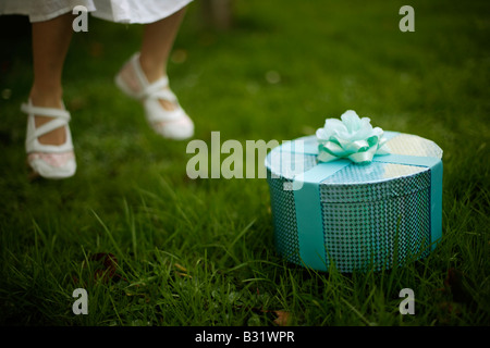 Fünf Jahre altes Mädchen mit grünen Box verpackt in Band und rose, springt in die Luft Füße über Boden Stockfoto