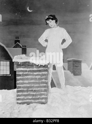 Junge Frau, die am Schornstein auf verschneiten Dach Stockfoto