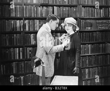 Profil eines jungen Mannes Anbringen einer Brosche auf eine junge Frau den Mantel in einer Bibliothek Stockfoto