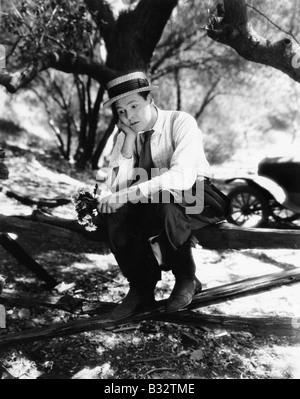 Mann sitzt auf einem Zaun mit Blumen in den Händen und schauen traurig Stockfoto