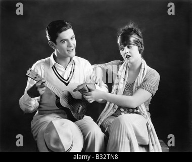 Junger Mann hält eine Gitarre mit einer jungen Frau, die ihm beizubringen, wie man spielen Stockfoto