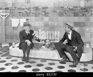 Zwei Männer sitzen am Rand der Badewanne in Anzügen und schrubben eine Freunde zurück Stockfoto