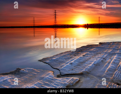 Sonnenaufgang-Salz Wohnungen Powerlines Spiegelung Wasser ruhig Stockfoto