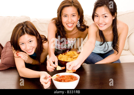 Drei attraktive asiatische Frauen Essen Chips auf dem sofa Stockfoto