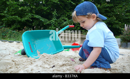 kleiner Junge in einer Sandbox Spiel mit Hand barrow Stockfoto