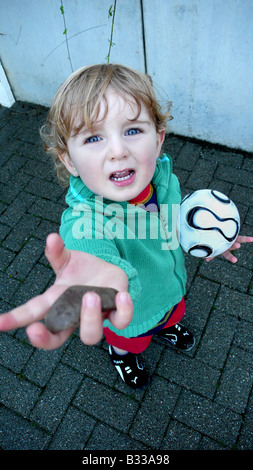 kleiner Junge mit Ball zeigt Stein Stockfoto