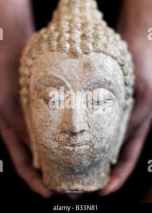 Eine Nahaufnahme der weiblichen Hände halten eine Statue eines Buddha-Kopf Stockfoto