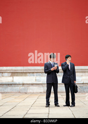 Zwei chinesische Geschäftsleute in Anzügen, die eine Diskussion auf dem Handy in der verbotenen Stadt. Stockfoto