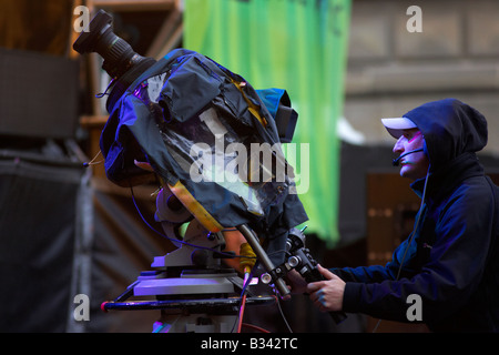 TV-Kameramann auf der Bühne mit Regenschutz auf Kamera filmt bei einem Outdoor-Gig beim Festival Belfast Nordirland Stockfoto