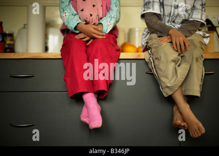 Sitzen auf der Küche Arbeitsplatte Mädchen im Alter von fünf und sechs Uhr-Zubereitung Bruder Stockfoto