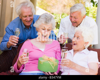 Zwei Paare auf Terrasse mit Champagner und Geschenk lächelnd Stockfoto