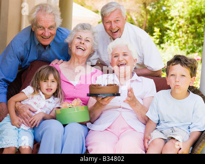 Großeltern und Enkelkinder auf Terrasse mit Kuchen und Geschenk lächelnd Stockfoto