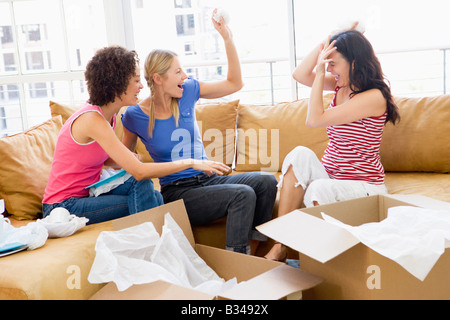 Drei Freundinnen, die spielerisch Auspacken Boxen im neuen Hause lächelnd Stockfoto