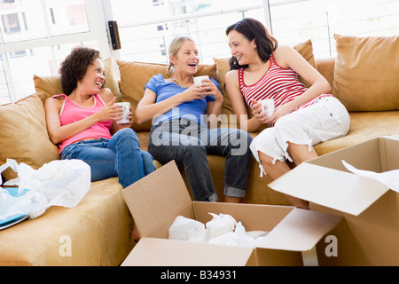 Drei Freundinnen entspannen mit Kaffee von Boxen im neuen Hause lächelnd Stockfoto