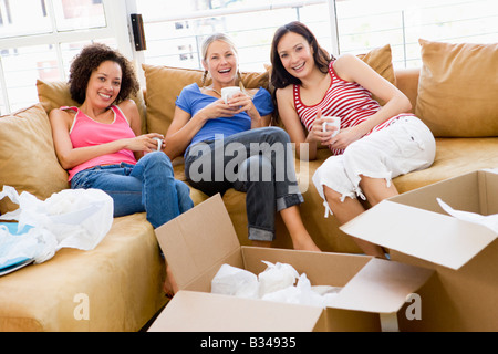 Drei Freundinnen entspannen mit Kaffee von Boxen im neuen Hause lächelnd Stockfoto